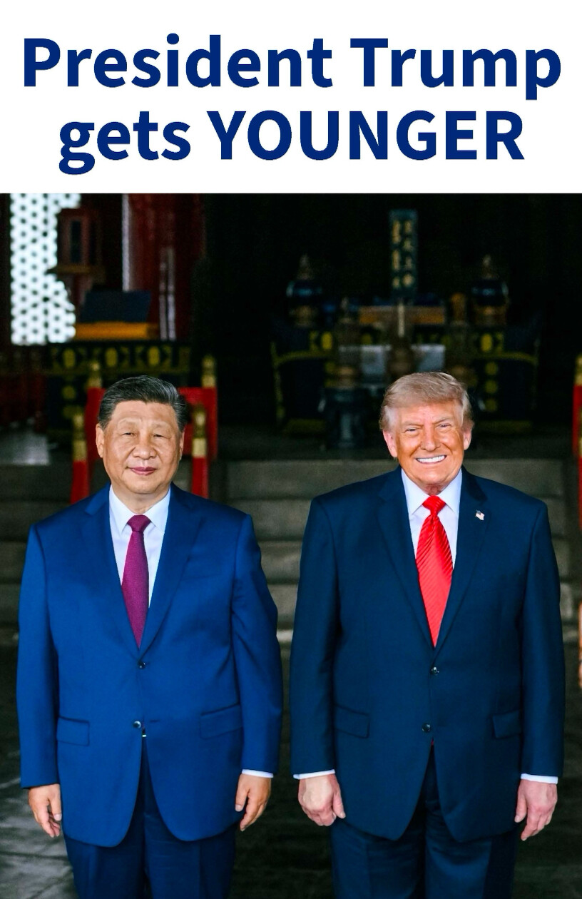 A photograph shows two men in formal suits standing side by side. The man on the left is wearing a blue suit with a red tie, while the man on the right is wearing a dark suit with a red tie. Above them is text in bold letters: "President Trump gets YOUNGER". The setting appears to be indoors with ornate decorations in the background.